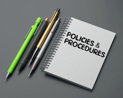 A photograph of a spiral-bound notebook with the words "policies and procedures" on it.
