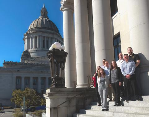 group of eight people standing on steps to legislative building with Capital dome visible in background